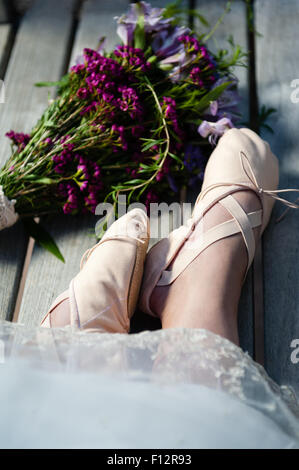 Frau die Füße in Schläppchen mit Spitzen Saum und einem nahe gelegenen Bouquet von Wildblumen. Stockfoto