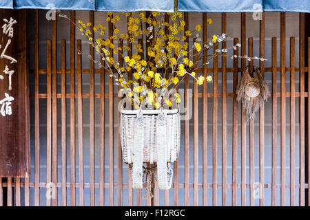 Tsumago, Japan. Straße von Terashita, geflochtenen Korb außenrolläden von Inn mit Filialen und gelbe Blumen, und eine blaue noren Vorhang oben hängen. Stockfoto