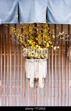 Tsumago, Japan. Straße von Terashita, geflochtenen Korb außenrolläden von Inn mit Filialen und gelbe Blumen, und eine blaue noren Vorhang oben hängen. Stockfoto