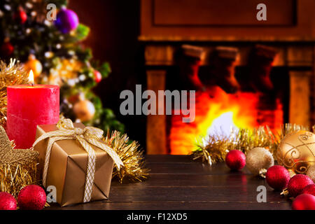 Weihnachtsschmuck, ein Geschenk und eine Kerze vor einem Kamin. Brennt ein Feuer im Kamin und Weihnachtsstrümpfe ein Stockfoto