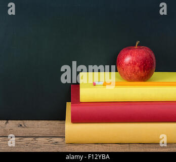 Roter Apfel mit einem Bleistift auf dem Stapel Schulbücher. Tafel im Hintergrund mit Textfreiraum. Stockfoto