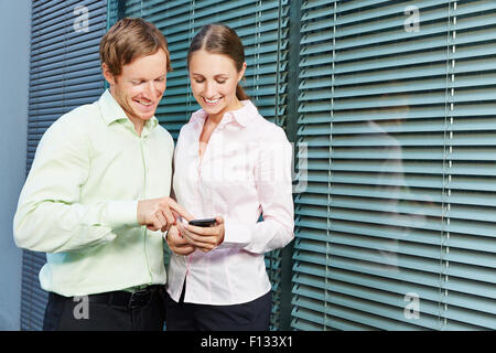 Zwei junge Geschäftsleute, die mit einer app auf dem Smartphone zusammen Stockfoto