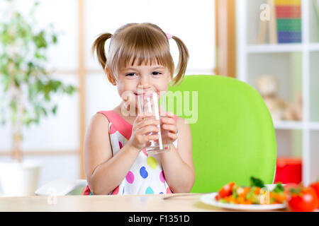 Lächelnde niedliche Mädchen hält Glas Wasser zu Hause Stockfoto