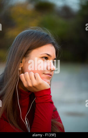 Junge Frau sucht Musik hören mit Kopfhörern Park, das Tragen der roten Pullover Stockfoto