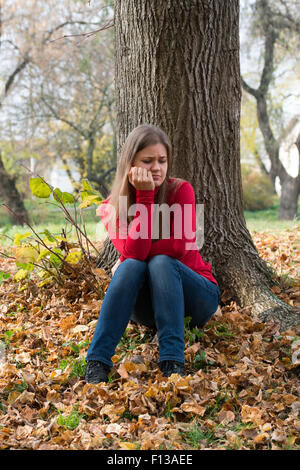 traurige junge Frau trägt rote Pullover, sitzen auf dem Boden im Herbst park Stockfoto