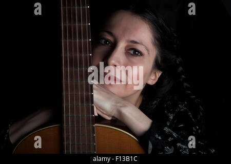Schöne nachdenkliche Frau stützte sich auf Gitarrenhals (Closeup Portrait über schwarz, warmen Tönen) Stockfoto