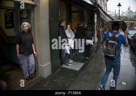 London, UK. Sonntag, 23. August 2015. Schwere Regen Sommerduschen im West End. Menschen mutig die Nässe, bewaffnet mit Sonnenschirme und wetterfeste Kleidung. Zigarettenpause unter dem Deckmantel in Covent Garden. Stockfoto