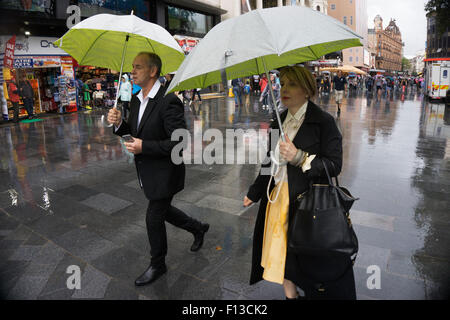 London, UK. Sonntag, 23. August 2015. Schwere Regen Sommerduschen im West End. Menschen mutig die Nässe, bewaffnet mit Sonnenschirme und wetterfeste Kleidung. Leicester Square. Stockfoto