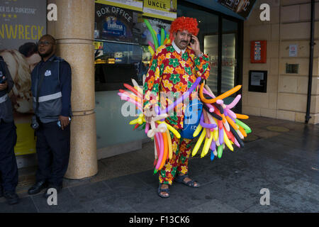 London, UK. Sonntag, 23. August 2015. Schwere Regen Sommerduschen im West End. Menschen mutig die Nässe, bewaffnet mit Sonnenschirme und wetterfeste Kleidung. Ballonmann nimmt Zuflucht am Leicester Square. Stockfoto