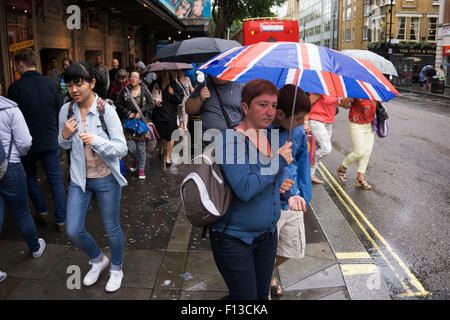 London, UK. Sonntag, 23. August 2015. Schwere Regen Sommerduschen im West End. Menschen mutig die Nässe, bewaffnet mit Sonnenschirme und wetterfeste Kleidung. Union Jack-Flagge-Regenschirm. Stockfoto