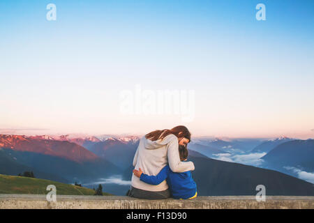 Rückansicht der Frau sitzt auf einer Mauer, die ihren Sohn umarmt Stockfoto