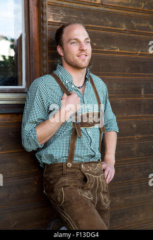 junger Mann in bayerischen Lederhosen eine hölzerne Wand gelehnt Stockfoto