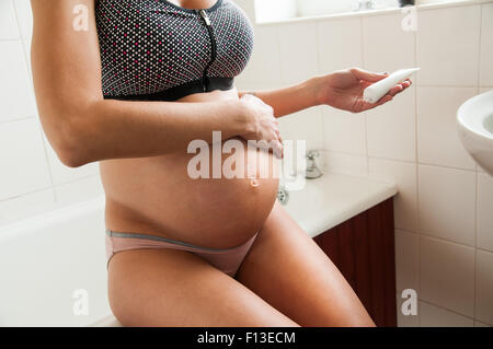 Schwangere Frau Feuchtigkeitscreme auf den Bauch reiben Stockfoto