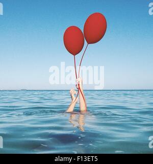 Menschliche Hände kommen aus dem Meer halten zwei Ballons Stockfoto