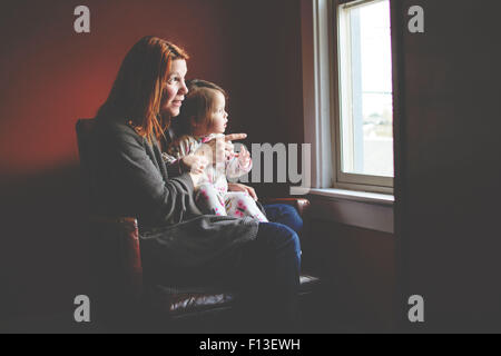 Babymädchen sitzen auf der Mutter Schoß, schaut aus dem Fenster Stockfoto