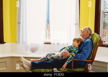 Junge sitzt auf seinem Großvater Schoß entspannend Stockfoto