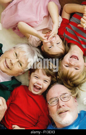 Blick von oben auf drei Kinder, die mit ihren Großeltern auf dem Boden liegen Stockfoto