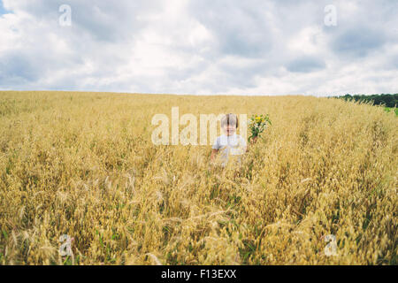 Fröhlicher Junge stehend in einem Feld hält eine Reihe von Wildblumen Stockfoto