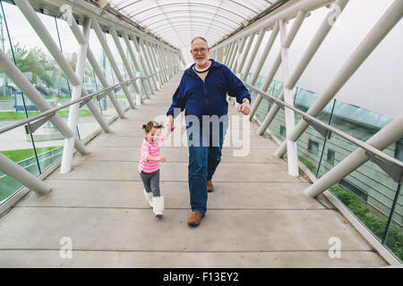 Mädchen und ihr Großvater Hand in Hand, zu Fuß über einen Gehweg Stockfoto