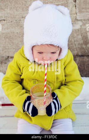 Mädchen im Winter draußen sitzen und einen Milchshake trinken Stockfoto