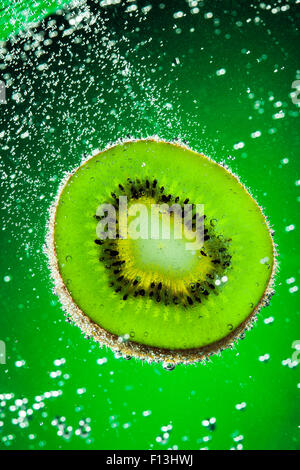 Frische Kiwi fällt im Wasser auf einem grünen Hintergrund Stockfoto