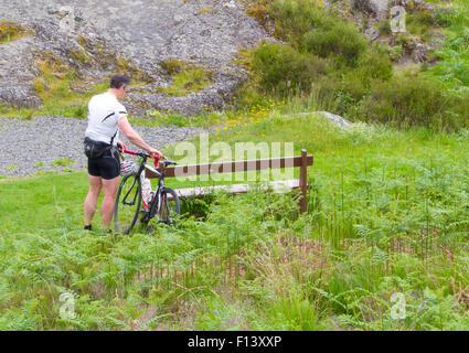Radfahrer, die Demontage einer ruht sein Fahrrad gegen eine Bank, Glen Trool, Galloway Forest Park, Dumfries & Galloway, Schottland, UK Stockfoto