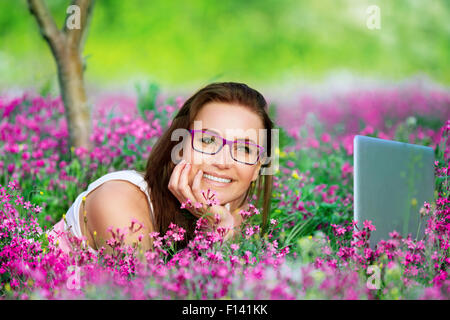 Porträt der schönen lächelnden Studentin liegend auf Blumen Wiese im Garten Universität Stockfoto