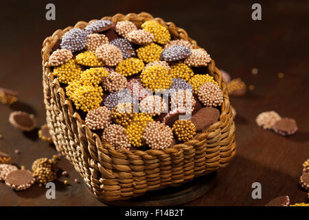 Bunte Schoko Dragees im Korb auf einem hölzernen Hintergrund platziert Stockfoto