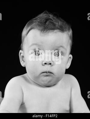 1950ER JAHRE WEIT AUFGERISSENEN AUGEN MOLLIG WANGE BABY MACHEN LUSTIGE MIMIK, BLICK IN DIE KAMERA Stockfoto