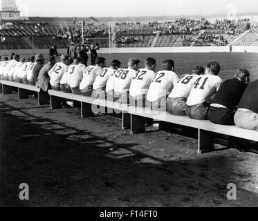 1940ER JAHRE HIGH SCHOOL ODER COLLEGE FOOTBALL TEAMS HINTER ALLE SITZEN AUF DEN BÄNKEN DER SEITENLINIE Stockfoto