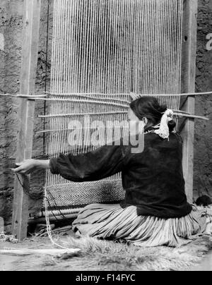 1930ER JAHREN INDIANISCHE NAVAJO FRAU SITZT AM WEBSTUHL WEBEN EINES TEPPICHS Stockfoto