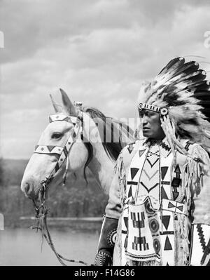 1920ER JAHRE PORTRAIT NATIVE AMERICAN INDIAN CHIEF VOLL FEDER KOPFSCHMUCK PERLEN KLEIDER PFERD STONEY SIOUX STAMMES ALBERTA KANADA Stockfoto
