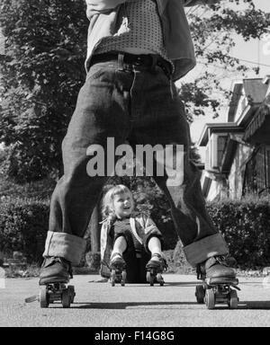 1950ER JAHRE MÄDCHEN GEFALLEN SITZEN BÜRGERSTEIG VERSCHLEIß METALL ROLLSCHUHE SCHUSS DURCH DIE BEINE JUNGE GEROLLTEN MANSCHETTE BLAU JEANS Stockfoto