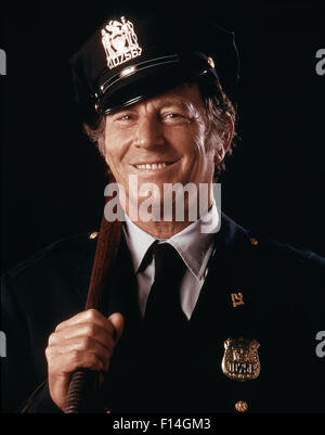 1970ER JAHRE PORTRÄT LÄCHELN FREUNDLICHE POLIZIST BLICK AUF KAMERA HOLDING GUMMIKNÜPPEL Stockfoto