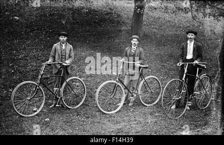 1900 1900S DREI DER 20. JAHRHUNDERTS MÄNNER POSIEREN STEHEND MIT DEM FAHRRAD, BLICK IN DIE KAMERA DREHEN Stockfoto