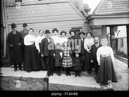 1890 1890S WENDE DES 20. JAHRHUNDERTS GRUPPE PORTRAIT FAMILIE DREI GENERATIONEN STEHEN ZUR SEITE DES HAUSES, BLICK IN DIE KAMERA POSIERT Stockfoto