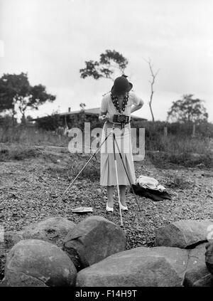 1930ER JAHRE ELEGANT GEKLEIDETE FRAU FOTOGRAF BLICK DURCH DEN SUCHER DER KAMERA AUF STATIV Stockfoto