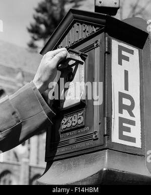 1920ER-1930ER JAHREN 1940ER JAHRE 1950ER JAHREN MÄNNLICHE HAND ZIEHEN HEBEL ON STREET FEUERALARM BOX Stockfoto