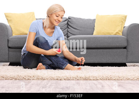 Junge Frau Polieren ihre Fußnägel sitzen auf dem Boden vor einem grauen Sofa isoliert auf weißem Hintergrund Stockfoto