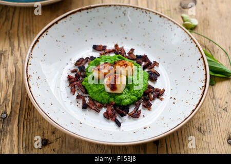 Jakobsmuscheln mit Erbsenpüree und knusprigem Speck Stockfoto