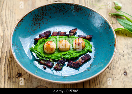 Jakobsmuscheln mit Erbsenpüree und knusprigem Speck Stockfoto