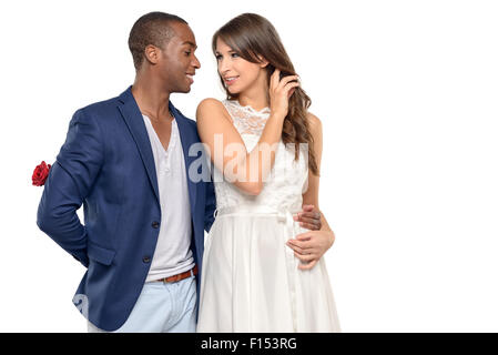 Romantischer junger Mann umarmt seine Freundin mit einem liebevollen Lächeln, als er verbirgt sich eine Überraschung Rot stieg hinter seinem Rücken, Valentinstag, Stockfoto