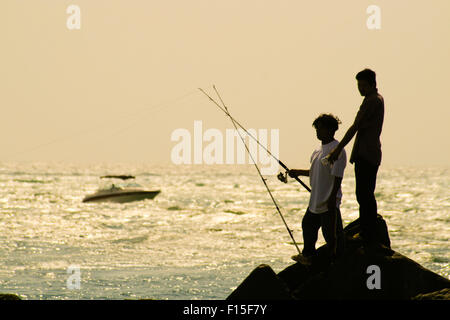 Nahaufnahme von zwei Fischern mit Ruten auf Felsen, Meer und Boot im Hintergrund, North Miami Beach, Florida. Stockfoto