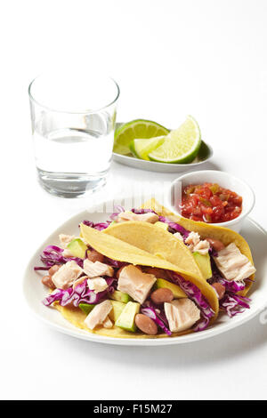 Thunfisch-Tacos mit Avocado, Kohl und Bohnen auf Teller, mit Salsa, Limetten und ein Glas Wasser, Studio gedreht auf weißem Hintergrund Stockfoto