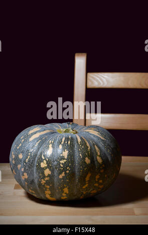 Einsame Kürbis auf rustikalen Kiefer Tisch mit Stuhl für Halloween oder Thanksgiving Vorbereitungen. Stockfoto