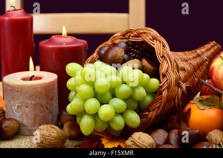 Happy Thanksgiving Tischdekoration in den klassischen rustikalen Farben auf Holztisch mit Füllhorn Herzstück, Kerzen und Obst. Stockfoto