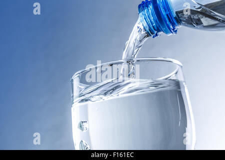 Gießt Wasser aus der Flasche ins Glas in blauen Tönen Stockfoto