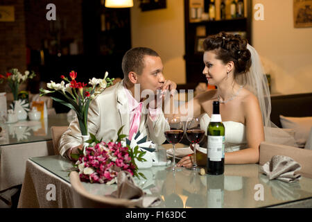 frisch verheiratetes Paar sitzt am Tisch im Restaurant, Romantik Hochzeitsessen, Kuss Stockfoto