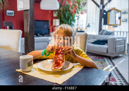 Blondschopf im gelben Trikot Essen an den Tisch Brot und Marmelade Stockfoto