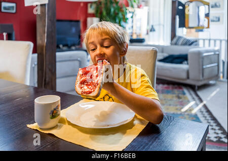 Blondschopf im gelben Trikot Essen an den Tisch Brot und Marmelade Stockfoto